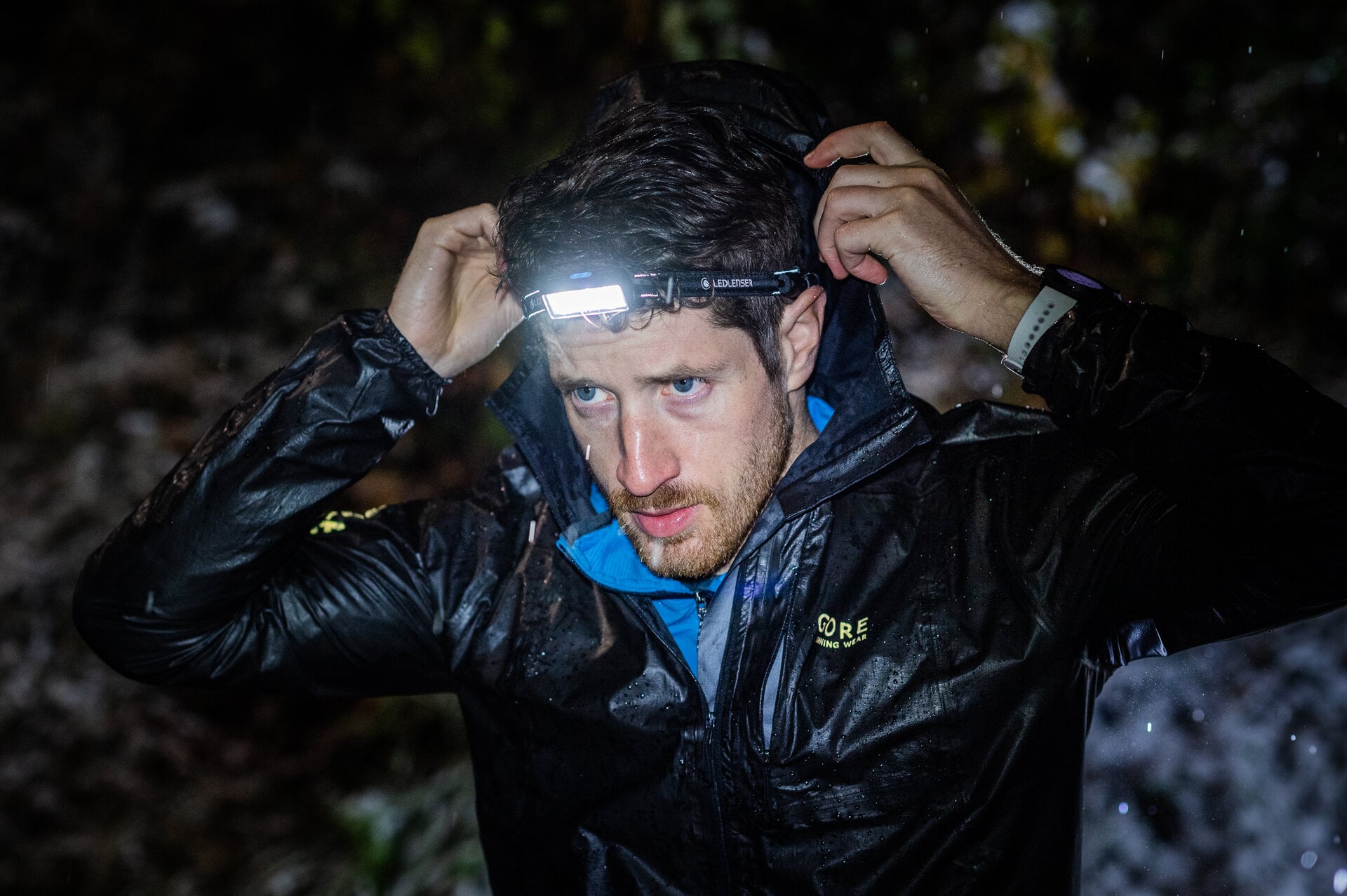 Trkač u mokroj jakni podešava čeonu lampu Ledlenser NEO9R po mraku i kiši